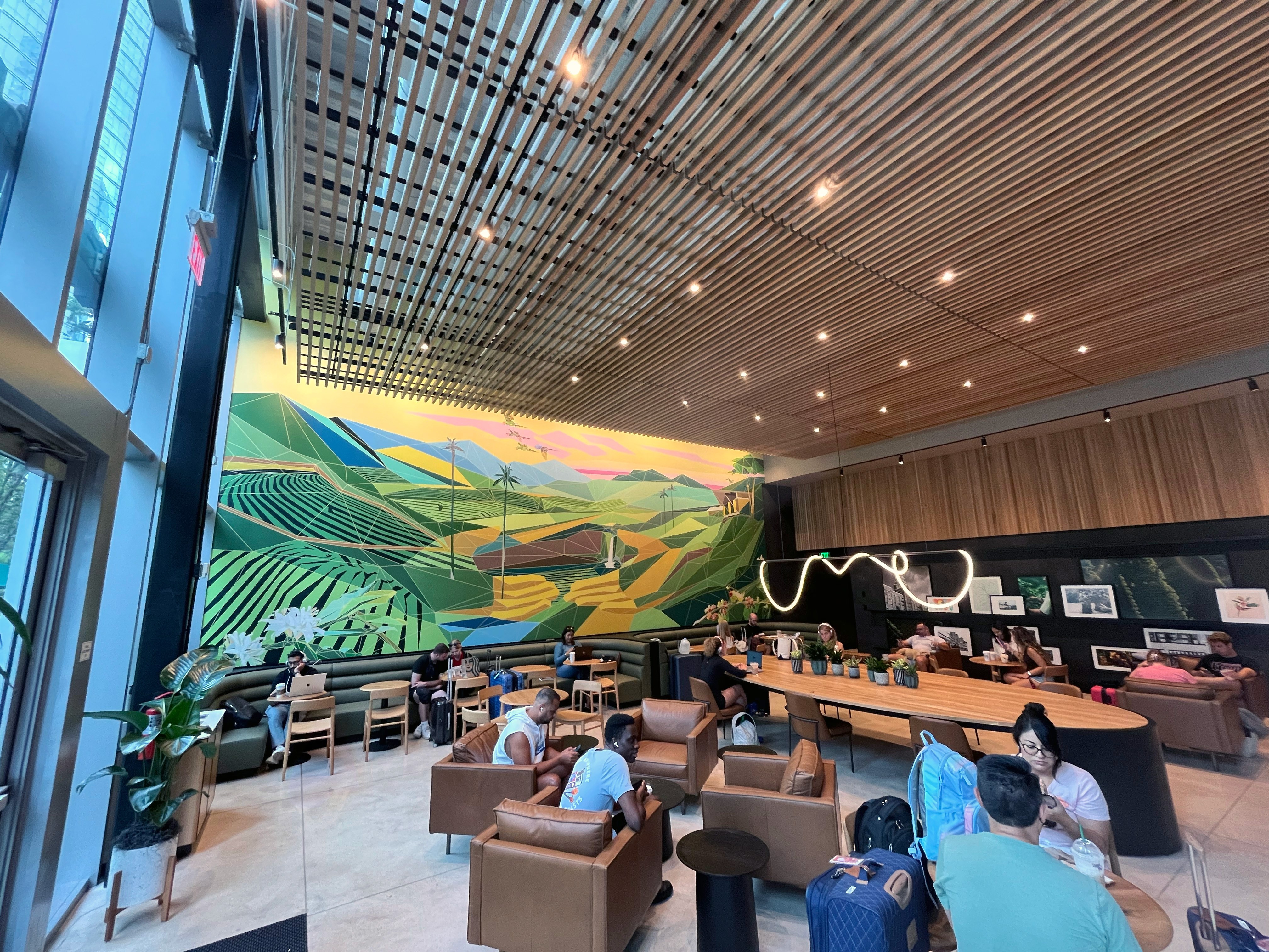A large geometric landscape mural inside a public space, with people working and gathering beneath it